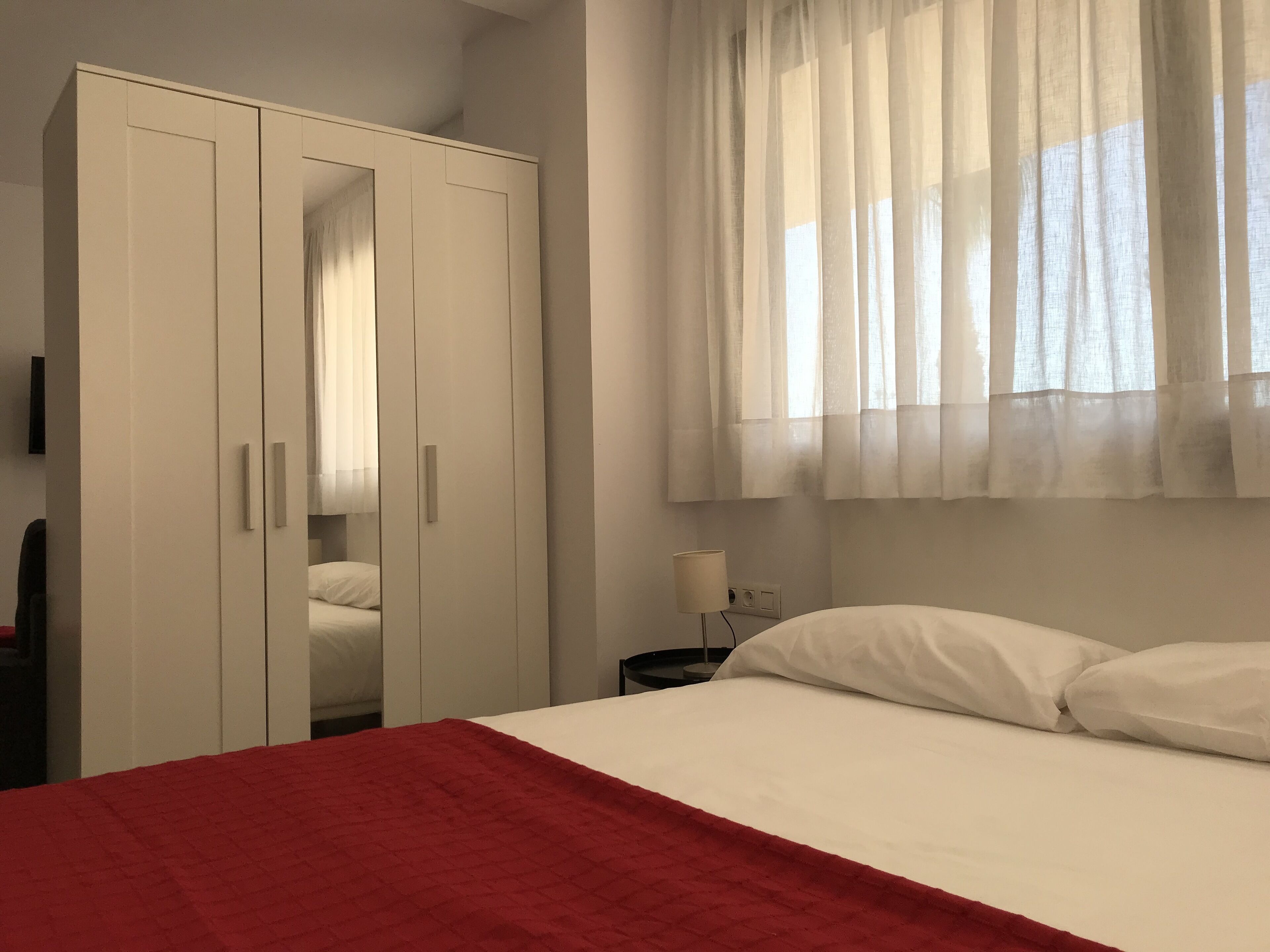 A bedroom with a bed, white curtains, and a wardrobe.