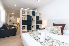 A modern hotel room with a large bed, a sofa, a desk, and a built-in storage unit. - Bet Apartments - City Suites Reig. (Valencia)