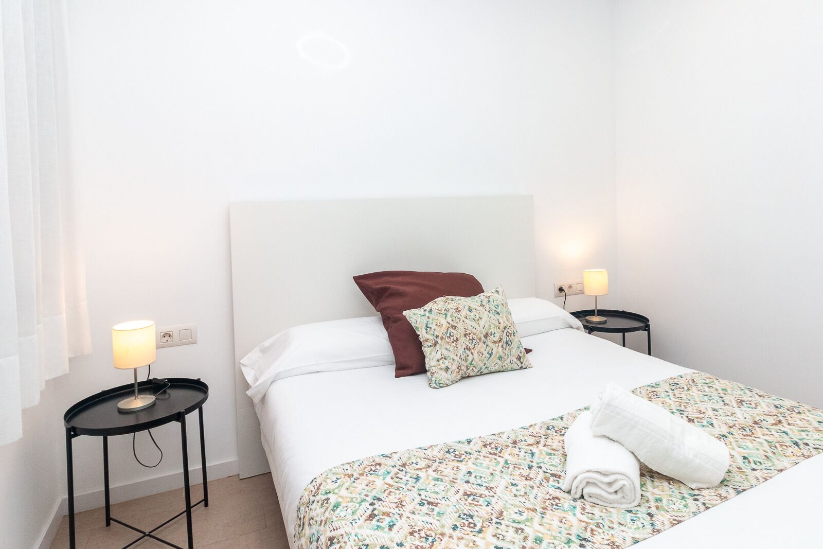 Habitación de hotel con una cama, dos mesitas de noche, una lámpara en cada una y una ventana con cortinas.