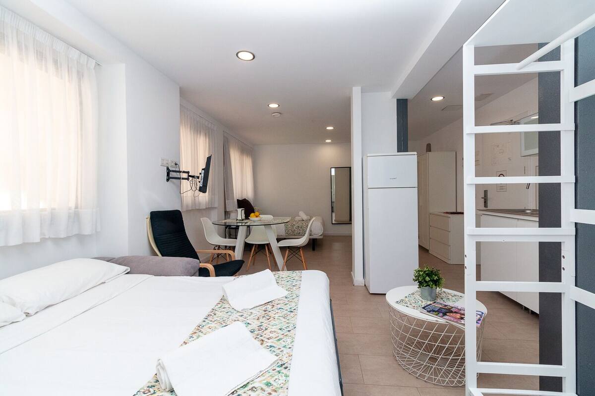 Ein modernes Hotelzimmer mit Bett, Schreibtisch, Stuhl, einem kleinen Tisch mit Pflanze und einem Kühlschrank.