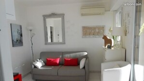 A living room with a grey sofa, red cushions, a white armchair, a small table with a vase, and a mirror on the wall. - Studio cabin sea view terrace, internet, air conditioned (Le lavandou)