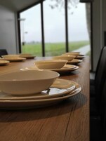 Una mesa de comedor con varios cuencos y platos, ubicada en una habitación con ventanas amplias y vista a un campo verde.