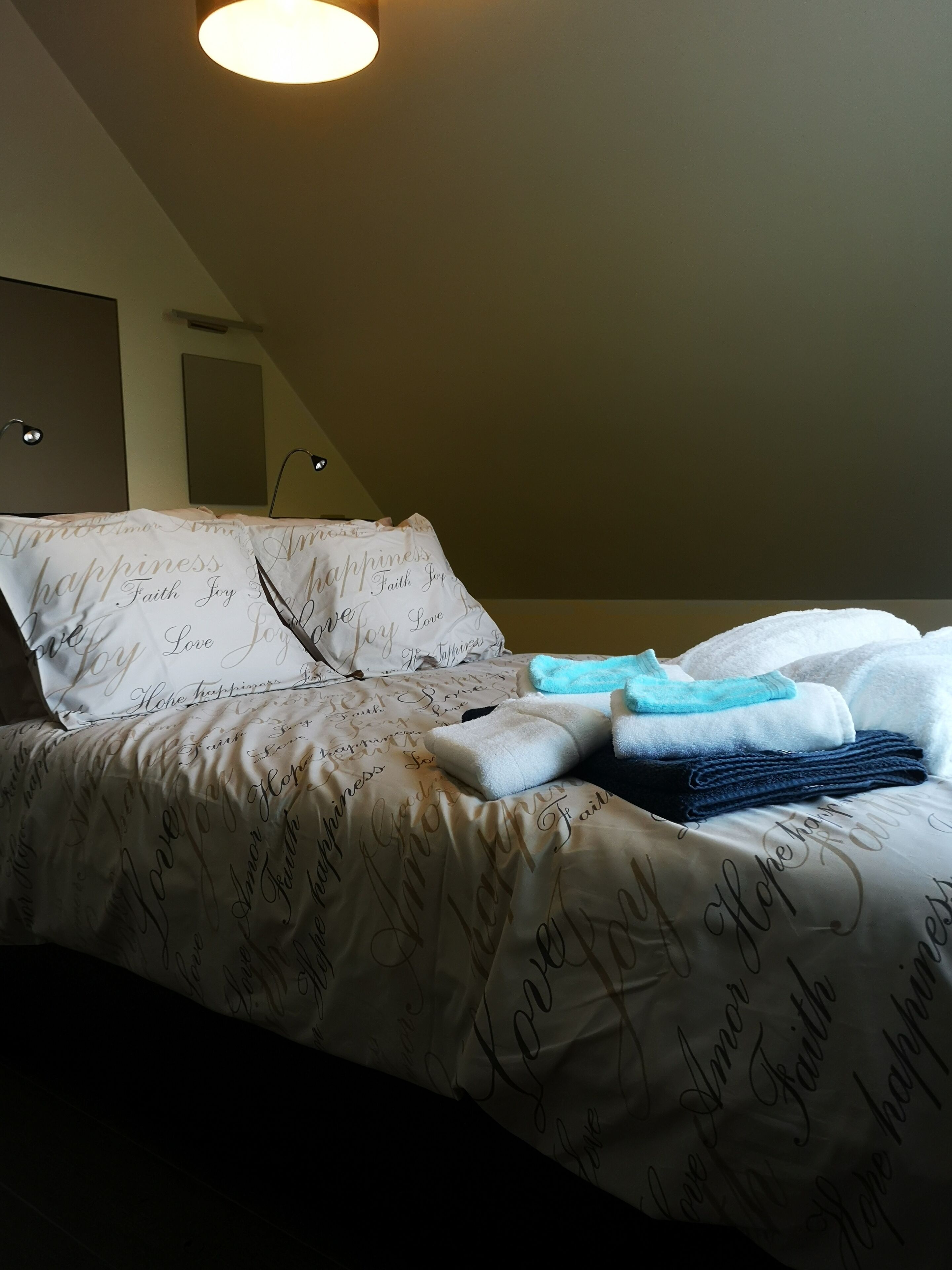 Een opgemaakt bed met een bedsprei met dessin, een bedlampje en gevouwen handdoeken.