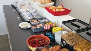Une table de buffet proposant divers aliments, notamment du pain, des pâtisseries et un saladier de fraises.