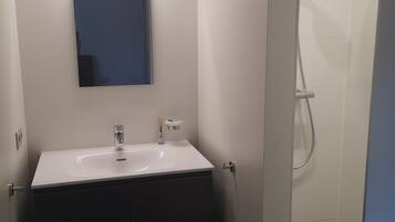 Een badkamer met een wit wastafel, een spiegel en een douche.