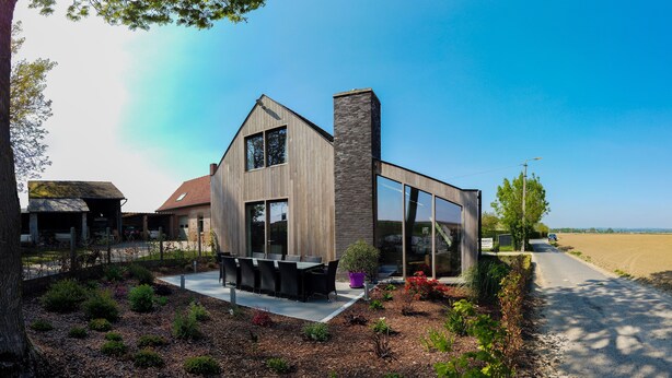 Une maison moderne dotée d’une grande baie vitrée, d’une terrasse en bois et d’un jardin.