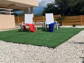 Relax in style with two lounge chairs surrounded by lush greenery and a wooden fence.