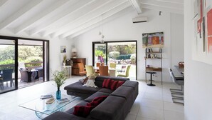 Ein geräumiges Wohnzimmer mit einer großen grauen Couch, einem Glastisch und Blick auf einen Garten durch große Schiebetüren.