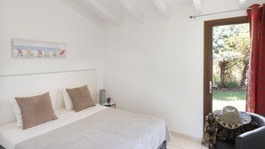 Ein Schlafzimmer mit einem Bett, einem Nachttisch, einem Fenster mit Blick auf Bäume und einer Tür.