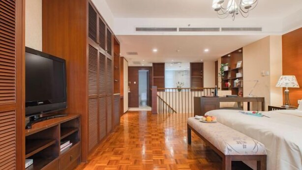 Une chambre d’hôtel avec un plancher en bois, une télévision, un lit avec une banquette et un escalier menant à une autre pièce.