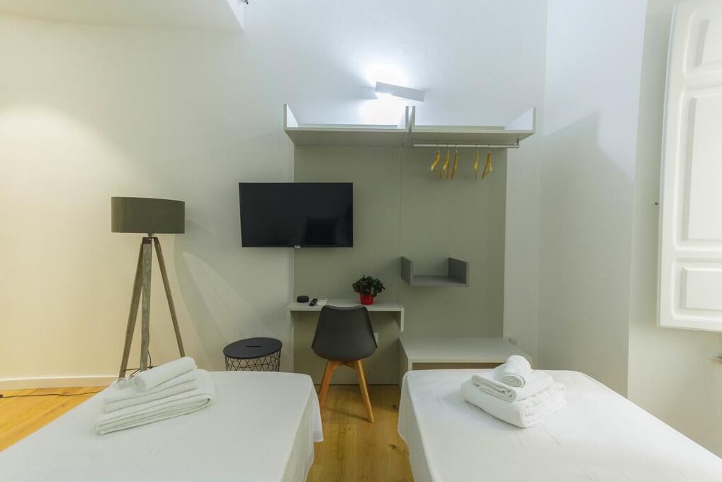 Camera d'albergo con due letti, una scrivania, una sedia, una televisione, una lampada e un piccolo vaso di fiori.
