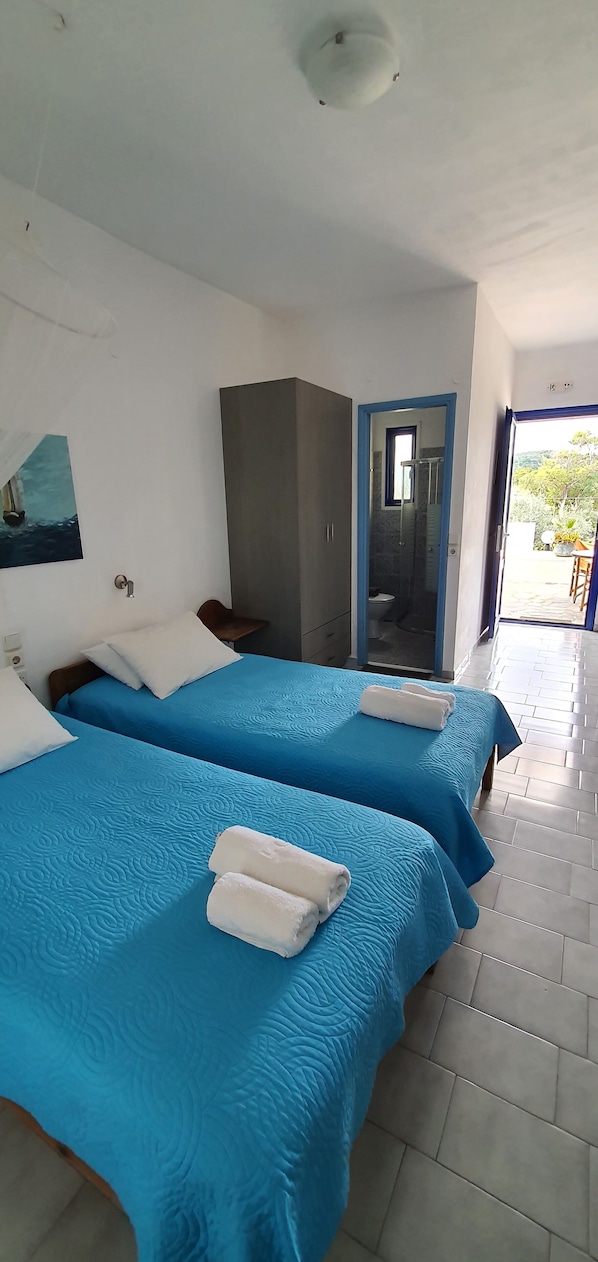 A hotel room with two beds, a wardrobe, a bathroom, and a view of the outdoors. - Irini Studios (Apokoronas)