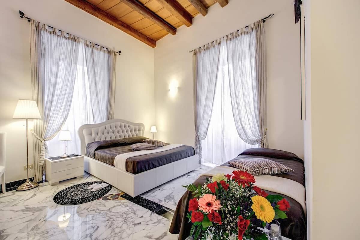 A bedroom with two beds, a nightstand, a lamp, and a floral arrangement.