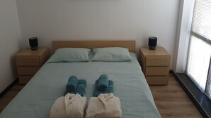 A bedroom with a bed, two bedside tables, a window with blinds, and a wall-mounted artwork of flowers. - Royal Bansko Aparthotel - 1 Bed Sleeps 4 (Bansko)