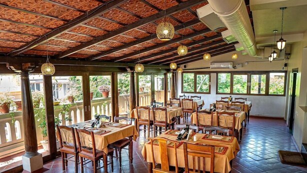 A restaurant with wooden tables and chairs, large windows, and hanging light fixtures. - Le Chateau - A Heritage Boutique Hotel (Pondicherry)