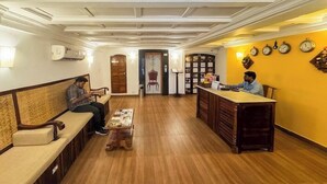 A hotel lobby with a wooden bench seating area, a reception desk, and a wall with clocks. - Le Chateau - A Heritage Boutique Hotel (Pondicherry)
