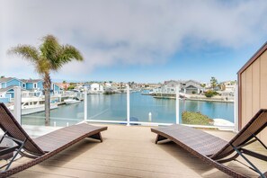 A balcony with wicker lounge chairs overlooking a marina with boats and houses. - Luxurious Channel Islands Harbor Home w/ Boat Dock (Oxnard)