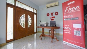Uma área de recepção com uma mesa de madeira, uma impressora e um grande anúncio promocional vermelho para OYO.