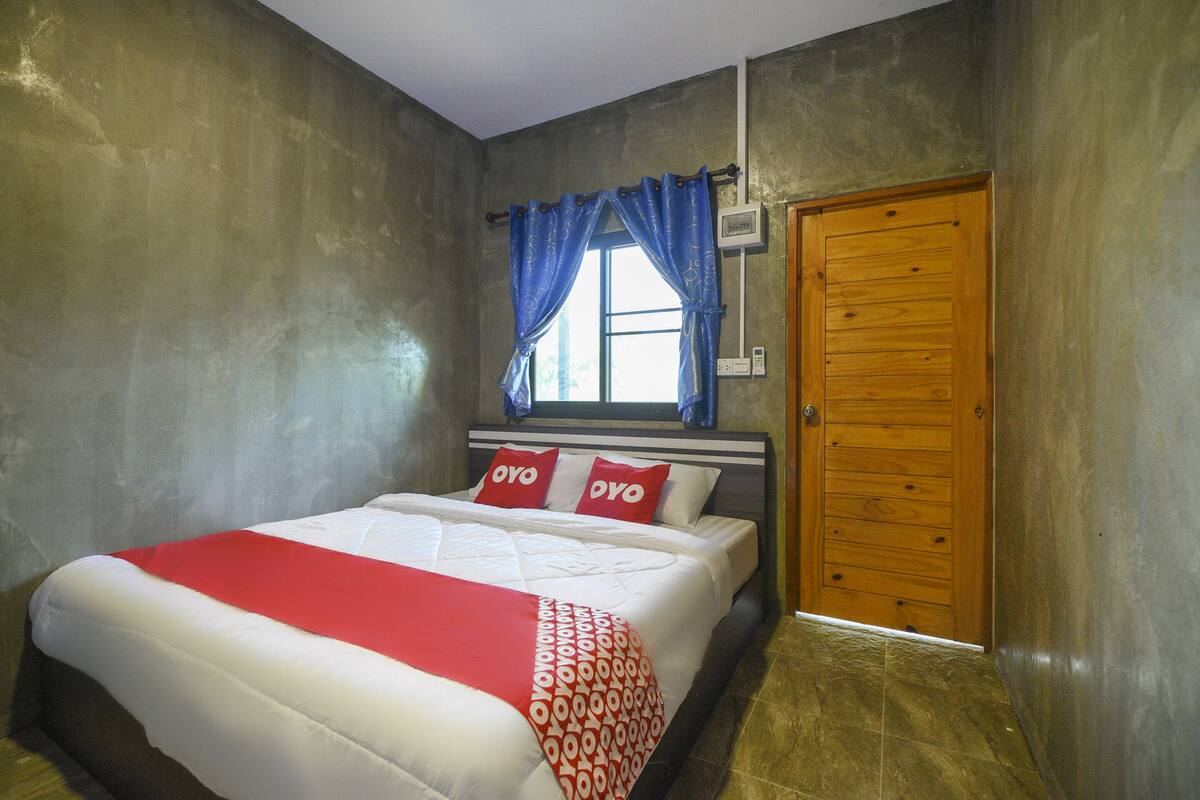 A bedroom with a bed, a window with curtains, a wooden door, and a wall-mounted air conditioning unit.