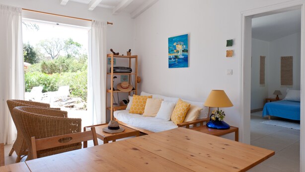 A cozy room with a wooden table, wicker chairs, a sofa with patterned cushions, and a view of greenery outside. - 3 bedroom house near Santa Giulia beach Residence heated swimming pool (Porto-Vecchio)
