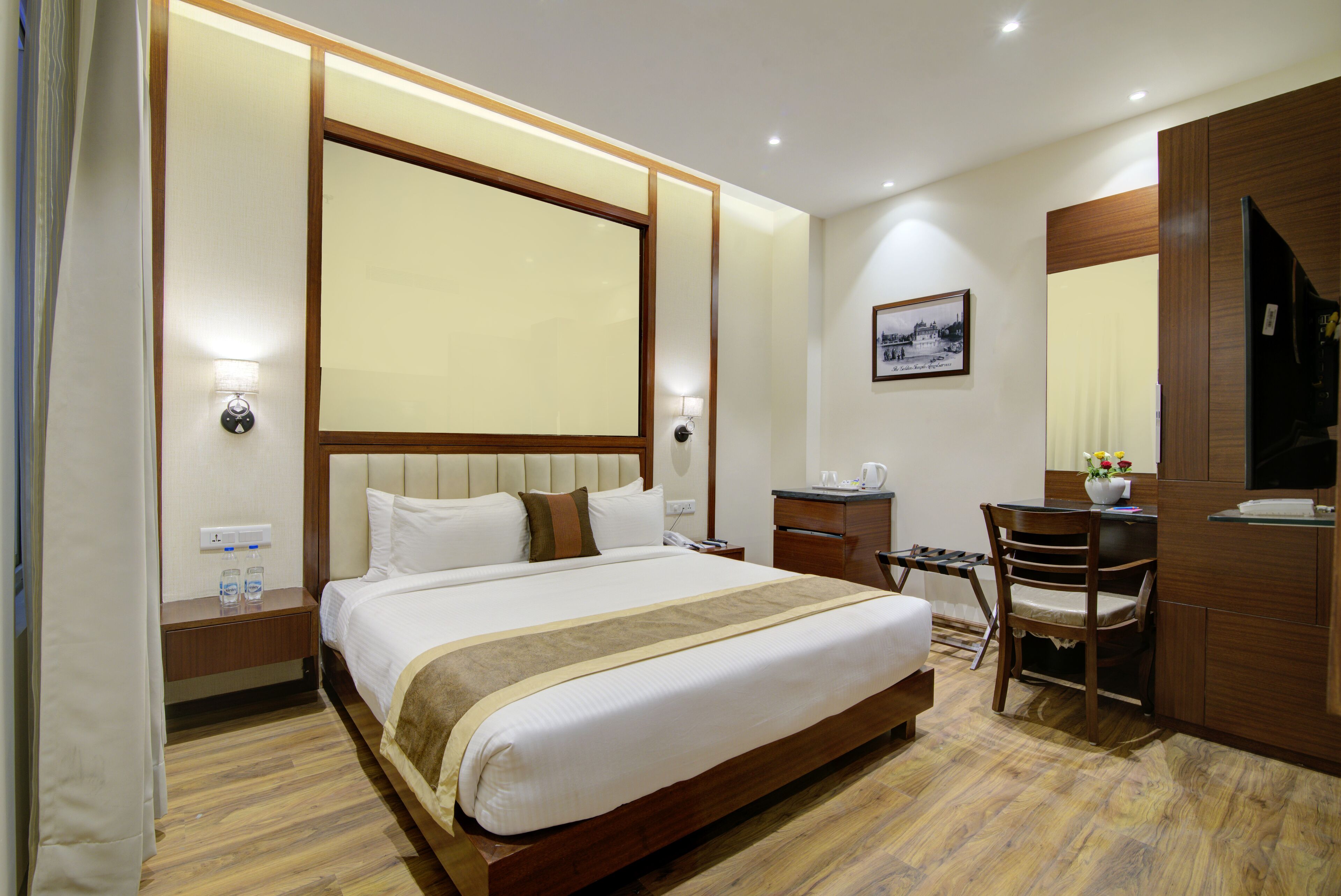 Une chambre d’hôtel avec un grand lit, des tables de chevet, un bureau avec une chaise, un miroir et un tableau encadré au mur.