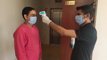 Une personne utilise un thermomètre frontal sur une autre personne dans un couloir où est affiché un panneau « Il est interdit de fumer ».