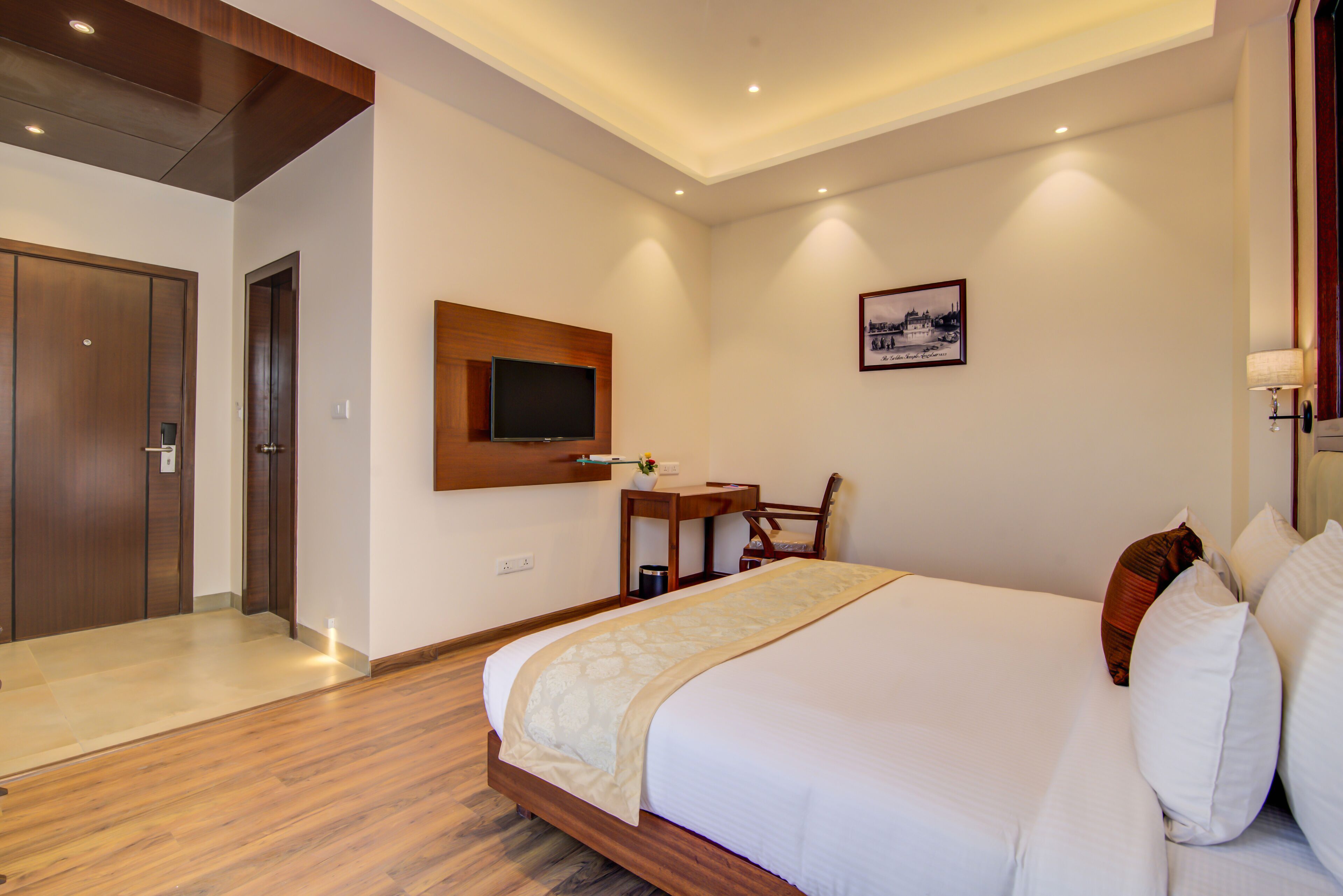 Una camera d'albergo con un letto grande, una scrivania con una sedia, un televisore a parete e un quadro incorniciato.