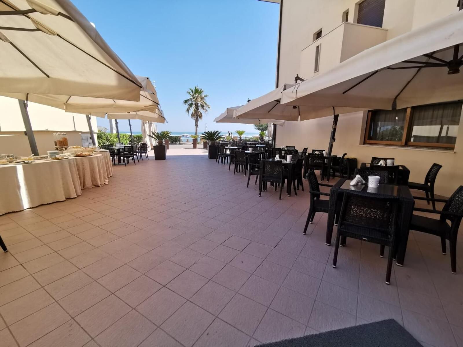 Un espace de restauration en plein air, avec des tables et des chaises, protégé par de grands parasols, et offrant une vue sur la mer en arrière-plan.
