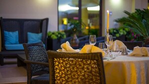 A dining area with wicker chairs, a table set with a candle, and a view of the outdoors. - Hotel Calgary (Casalbordino)