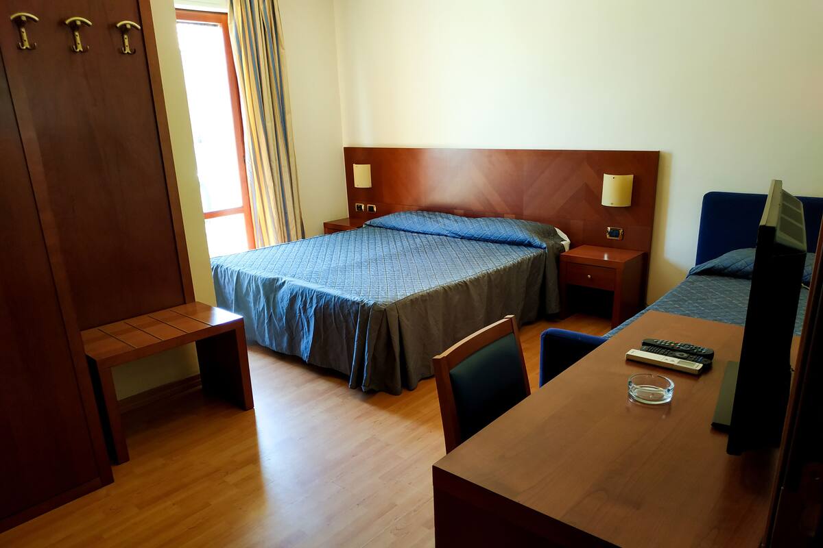 A hotel room with a wooden bed, a desk, a chair, and a TV.
