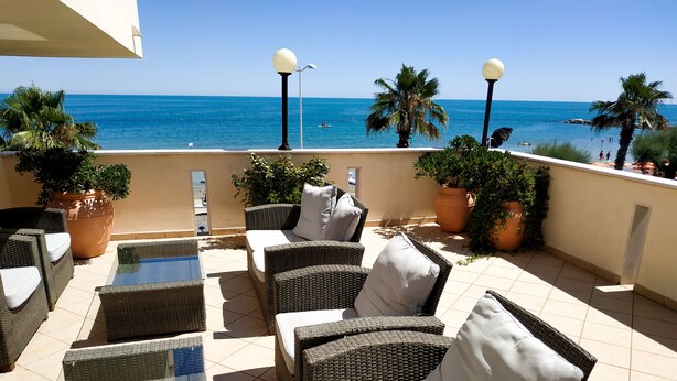 A terrace with wicker furniture, potted plants, and a view of the sea. - Hotel Calgary (Casalbordino)