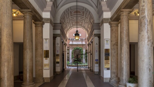 Un pasillo con columnas, piso de baldosas y una lámpara colgante.