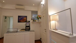 Habitación de hotel con minibar, cafetera, espejo y un cartel que dice 'Roman Nights'.