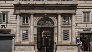 Fachada de un edificio histórico con un arco central, columnas y una reja metálica decorativa.