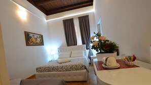 Habitación de hotel con una cama, un escritorio pequeño, una silla, un cuadro en la pared y una ventana con cortinas.