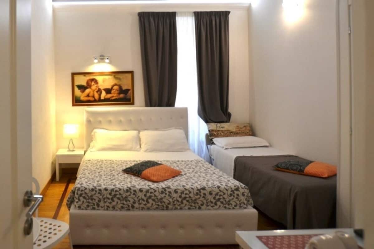 A bedroom with a large bed, two smaller beds, a nightstand, a lamp, and a painting on the wall.