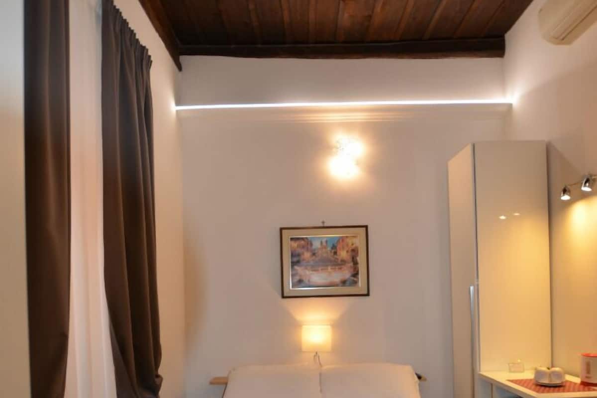 A bedroom with a bed, a desk, a mirror, and a painting on the wall.