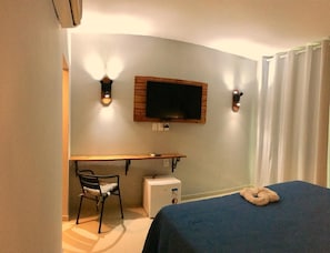 A hotel room with a bed, a desk, a chair, a television, and a small white appliance. - Antheia Ponta do Seixas (João Pessoa)
