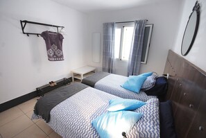 A bedroom with two beds, a small table, a bench, a radiator, and a wardrobe. - Cute little apartment close to promenade (Arinaga)
