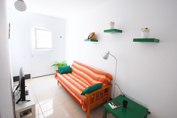 A bright living room with a sofa, a TV, a lamp, and green shelves with decorative items. - Cute little apartment close to promenade (Arinaga)
