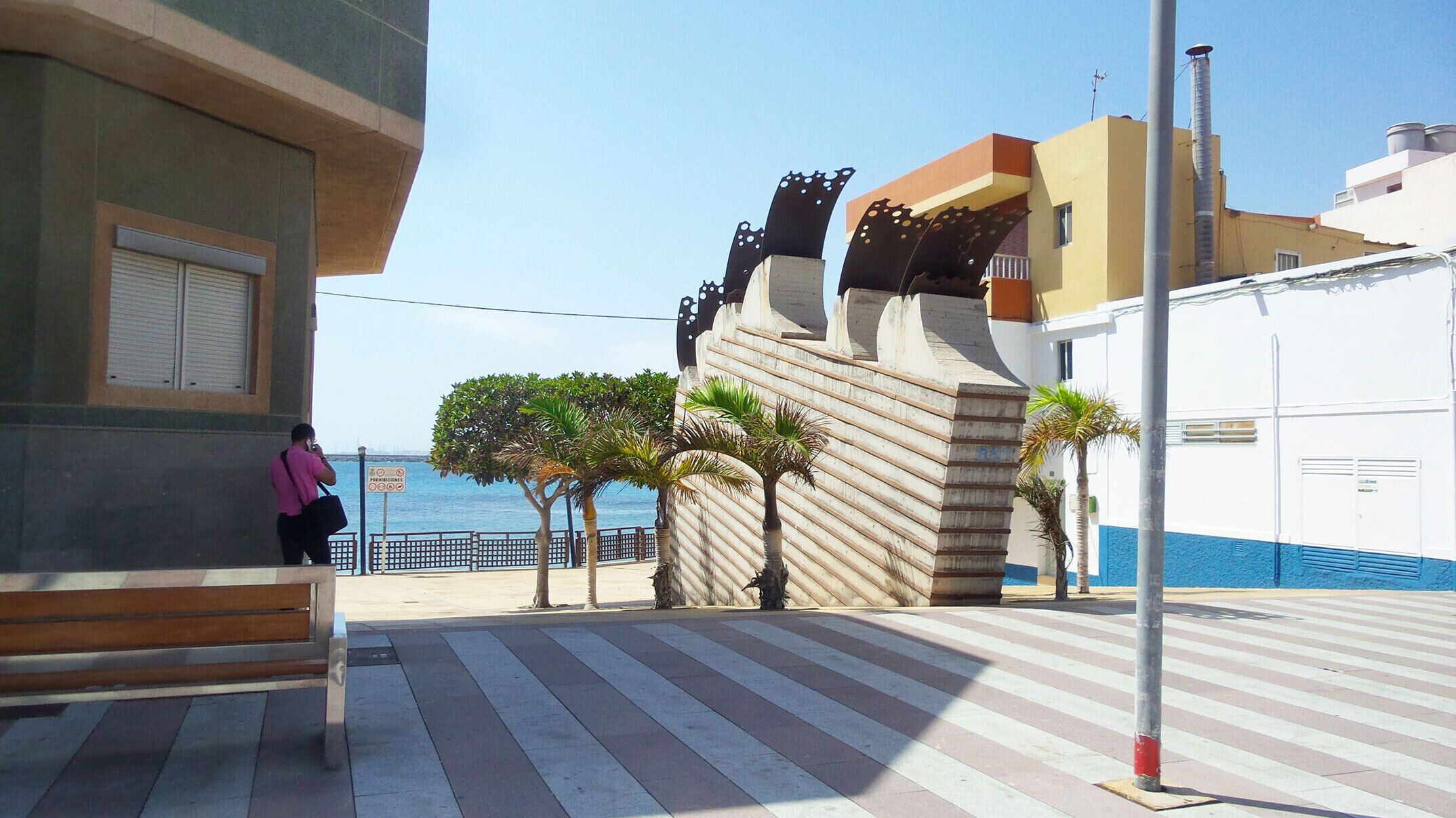 Une promenade en bord de mer, avec un banc, des palmiers et une vue sur la mer.