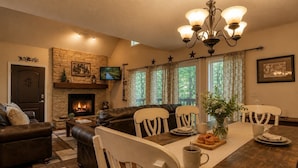 A cozy living room with a fireplace, a stone wall, a television, and a dining area with a table set for four.