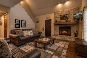 A cozy living room with a stone fireplace, leather sofa, and a patterned rug. - Moonshine Chalet, Hot Tub, Pool Access, WIFI,  $560 FREE tickets each paid day! (Gatlinburg)
