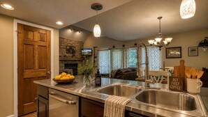 A kitchen with a double sink, wooden cabinets, a dishwasher, and a stone fireplace.
