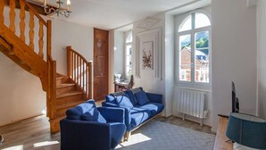 Een ruime woonkamer met een houten trap, een zithoek, een kroonluchter en een groot raam met uitzicht.