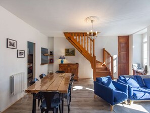 A dining area with a wooden table and chairs, a blue sofa, a wooden staircase, and a chandelier.