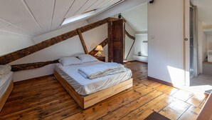 Een slaapkamer in loftstijl met een schuine kap, houten balken, een bed en een kleine tafel met een lamp.