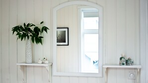 Une salle de bain avec des murs en bois peints en blanc, un grand miroir et deux étagères ornées d’objets décoratifs.