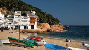 Une plage avec des bateaux, une falaise rocheuse et des bâtiments en arrière-plan.