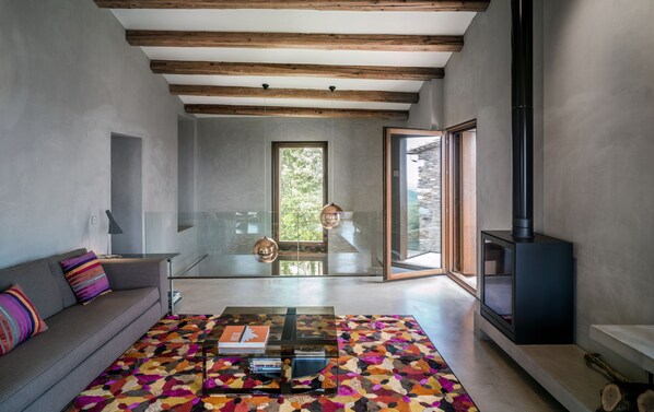 Una sala moderna con un sofá, una mesa de centro y un tapete colorido. Se ve un ventanal con vistas a zonas verdes.